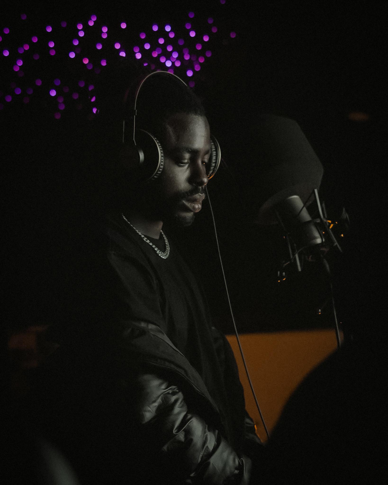 DERAA at the microphone in a darkened studio booth, headphones on