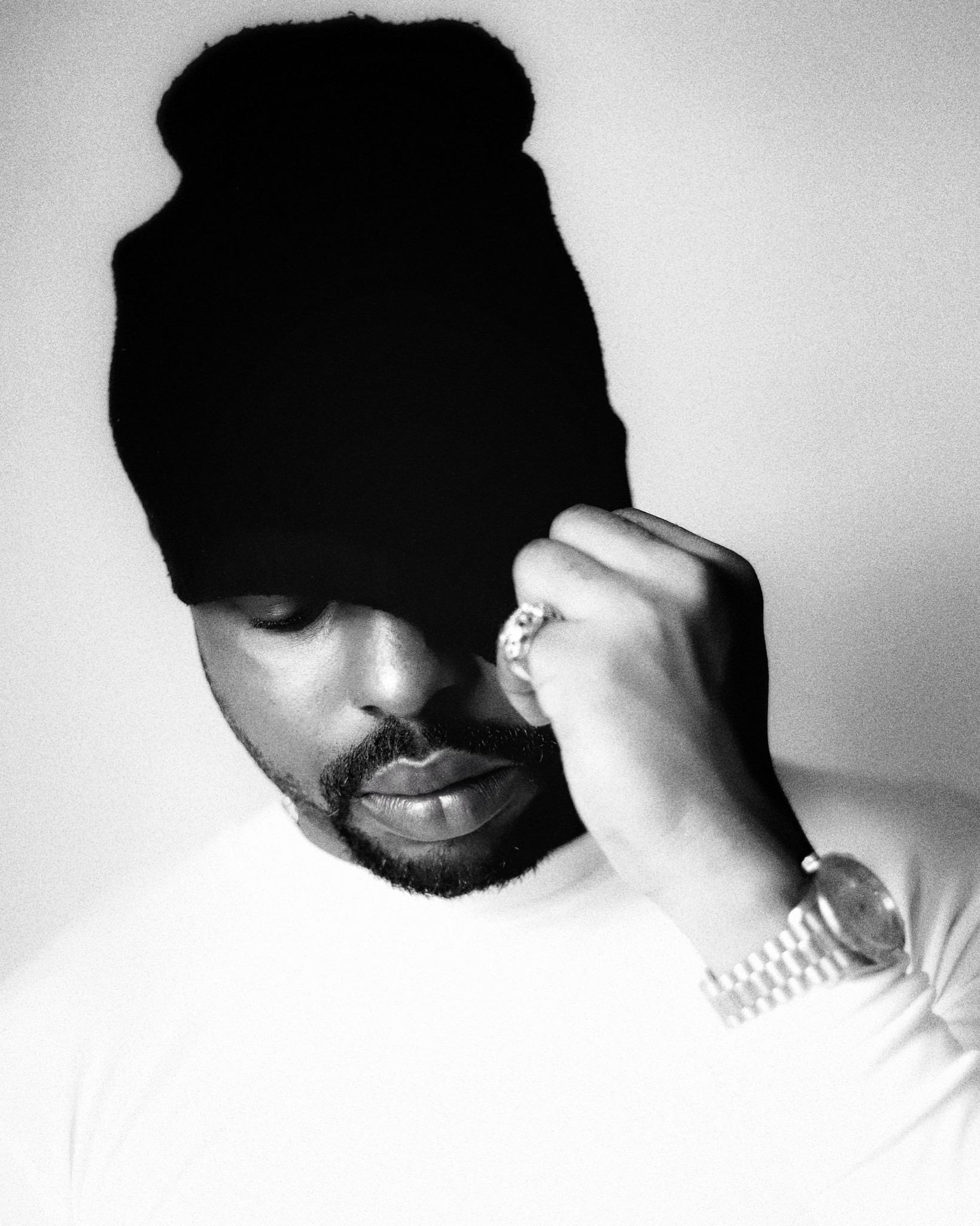 Black and white portrait of DERAA, beanie pulled low over his eyes